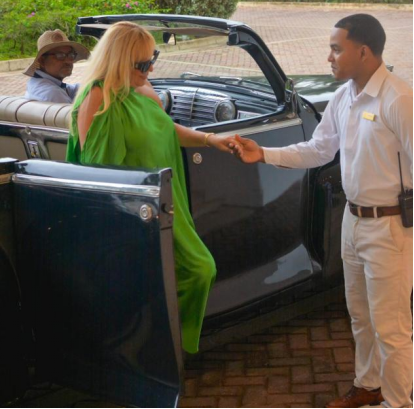 Valet assisting a passenger exiting a luxury car, while another person sits in the background.