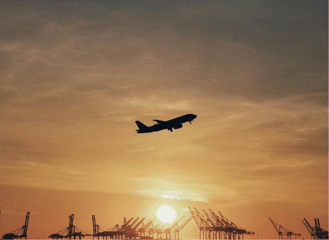 Aeroplane flying in early-morning sky at sunrise.